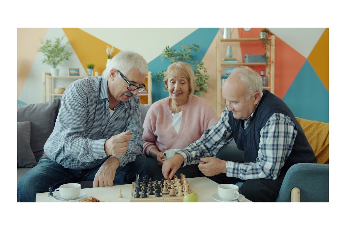 Three seniors playing chess together in a living room.