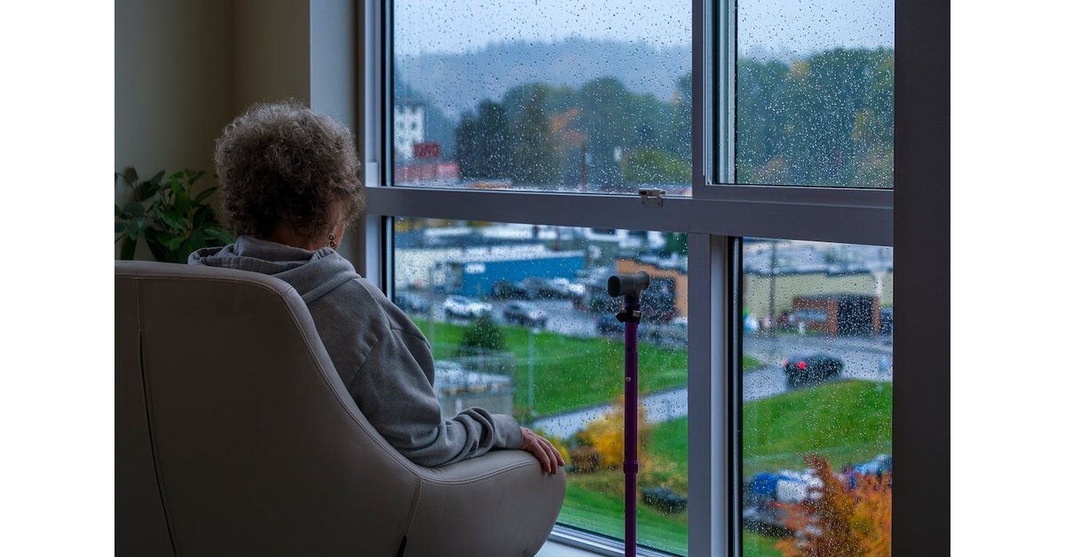 Woman sits in chair looking out rainy window