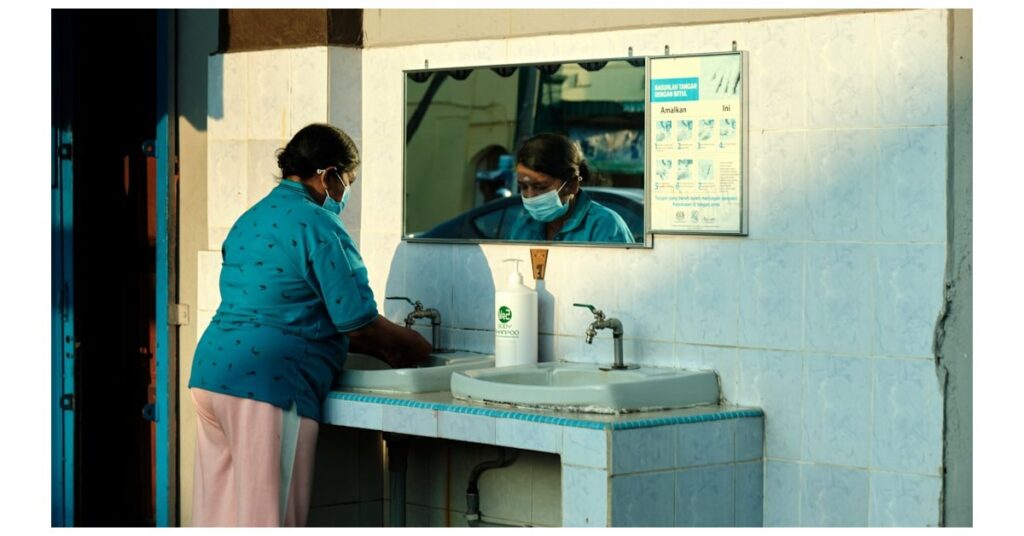 a woman wearing a face mask washes her hands in a sink