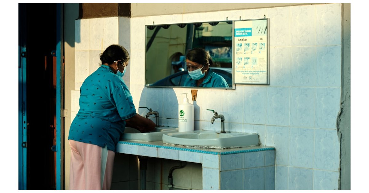 a woman wearing a face mask washes her hands in a sink